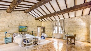 Una habitación rústica con paredes de piedra, techo de madera, cama, mesa y sillas.
