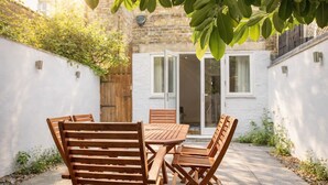 A patio with a wooden table and chairs, a white wall, and a door leading to a building. - Elegant 4-bed Apartment in Pimlico Sleep 7 (London)