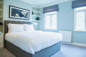 Quarto com cama grande, estantes embutidas, radiador e janela com cortina.