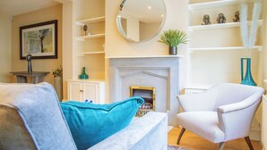 A living room with a fireplace, a round mirror, and a blue accent pillow. - Elegant 4-bed Apartment in Pimlico Sleep 7 (London)