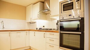 A kitchen with white cabinets, a stainless steel microwave, a double oven, and a wooden countertop. - Elegant 4-bed Apartment in Pimlico Sleep 7 (London)
