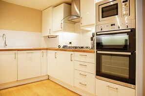 Eine Küche mit weißen Schränken, einer Edelstahl-Mikrowelle, einem Backofen mit Platz für zwei Auflaufformen und einer Holz Arbeitsplatte.