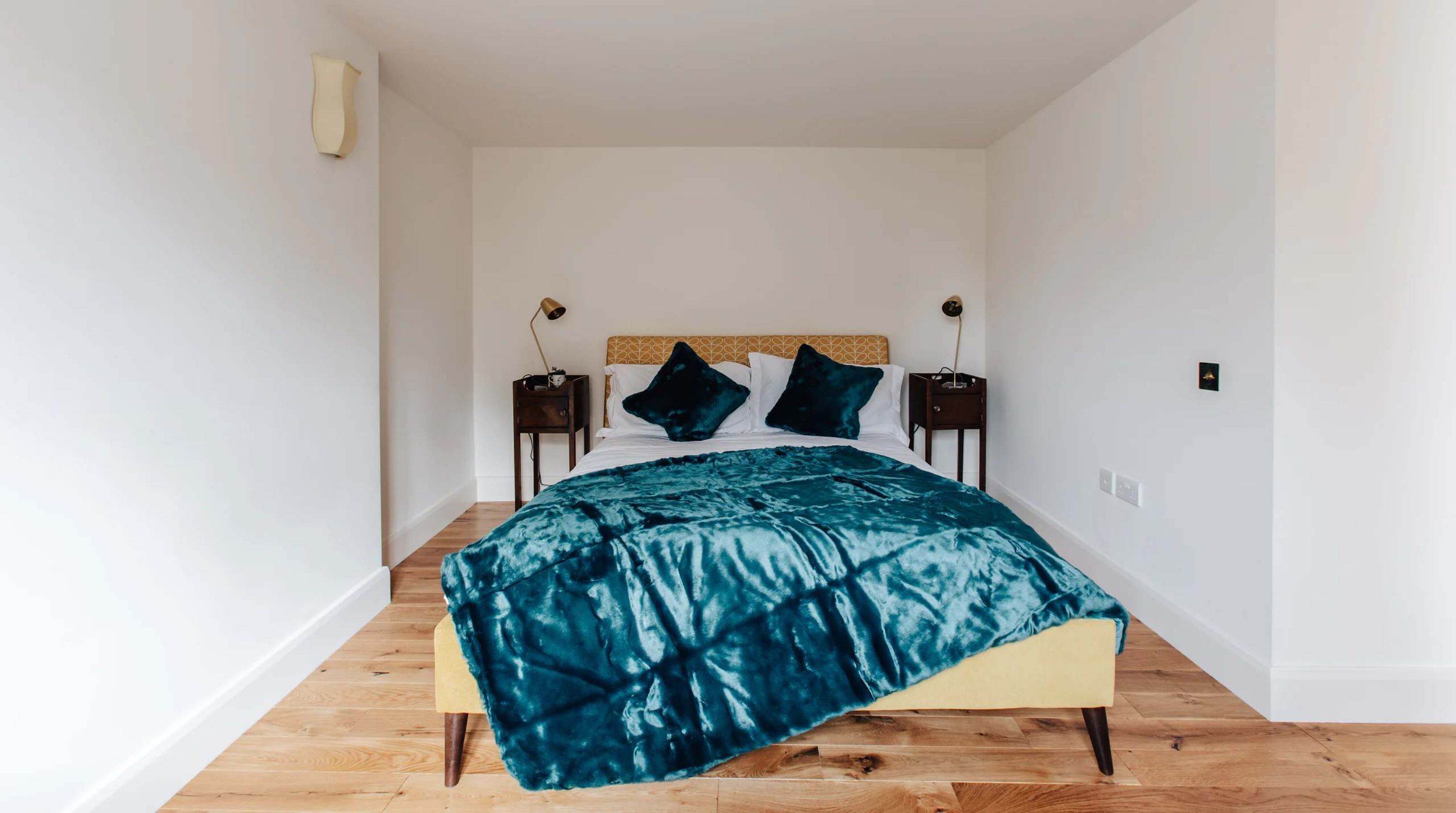 Ein Schlafzimmer mit einem Bett, Holzboden, weißen Wänden und zwei Nachttischen mit Lampen.