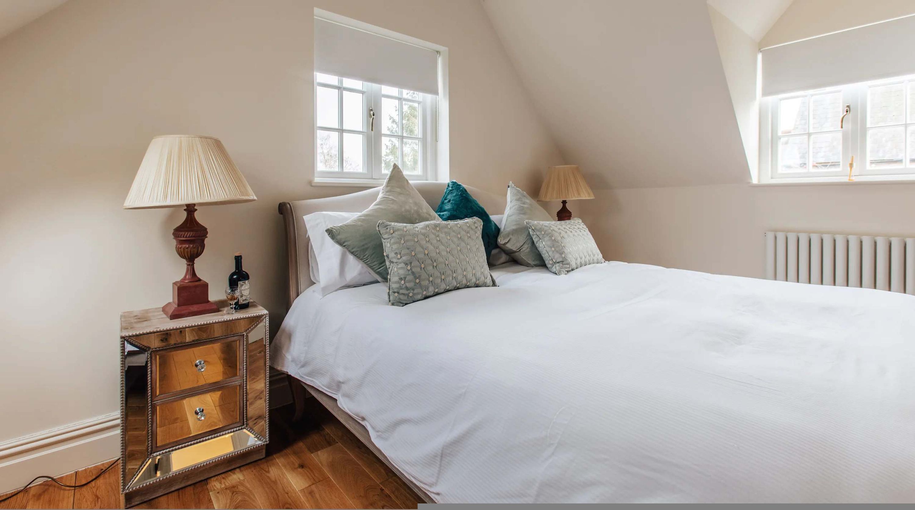 A bedroom with a bed, two bedside lamps, a wooden nightstand with drawers, and a window.
