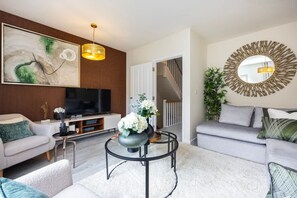 A modern living room with a flat-screen TV, a round coffee table, a sofa, and a decorative mirror. - Spacious Stylish 3-bedroom Home With Free Parking in Sw17 (London)