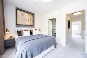 A bedroom with a bed, bedside tables, a large abstract painting, and a hallway leading to a bathroom. - Spacious Stylish 3-bedroom Home With Free Parking in Sw17 (London)