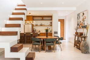 A modern kitchen with a central island, wooden staircase, and a dining area with chairs. - Designer Pool Luxury Escape Villa in Canggu (Jimbaran)