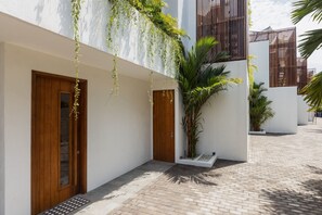 A building with a white exterior, wooden doors, a brick pathway, and a potted plant. - A Canggu Sojourn Villa (Cemagi)