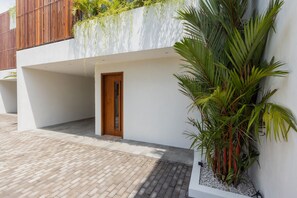 A modern building with a wooden door, white walls, and a palm tree. - A Canggu Sojourn Villa (Cemagi)