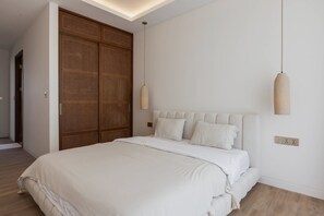 A bedroom with a large bed, wooden wardrobe, and pendant lights. - A Canggu Sojourn Villa (Cemagi)