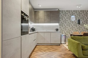 A modern kitchen with built-in appliances, a herringbone-patterned floor, and a dining area with a green sofa. - Spacious 2BR Near Stratford Station Olympic Park (London)