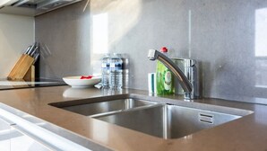 Una cocina moderna con electrodomésticos de acero inoxidable, un lavamanos doble y una encimera con un bloque para cuchillos y botellas de agua.