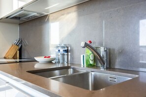 A modern kitchen with stainless steel appliances, a double sink, and a countertop with a knife block and water bottles. - Stylish 2-bed Apartment in Battersea (London)
