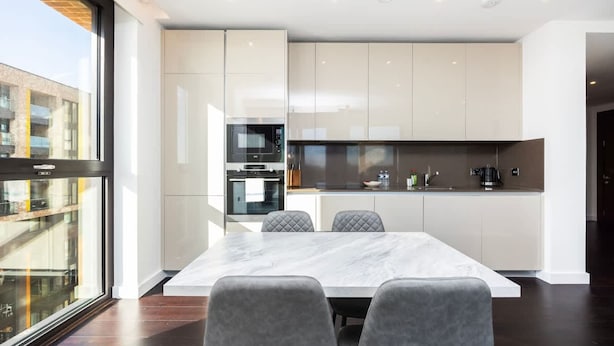 Una cocina moderna con encimera de mármol, electrodomésticos integrados y un comedor con una mesa grande y sillas acolchadas.