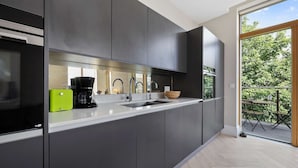 Una cocina moderna con armarios oscuros, encimera blanca, cafetera y un bol.