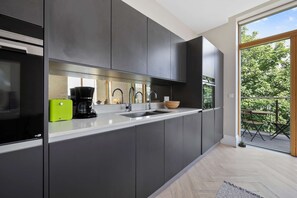 Eine moderne Küche mit dunklen Schränken, einer weißen Arbeitsplatte, einer Kaffeemaschine und einer Schüssel.