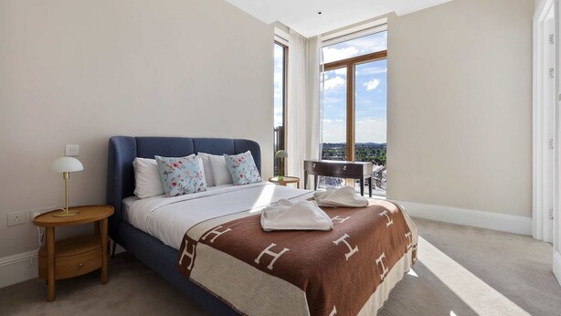 Un dormitorio con cama, mesita de noche, lámpara, vista al exterior y ventana.
