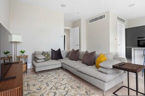 Ein modernes Wohnzimmer mit einem Ecksofa, einem Couchtisch, einer Lampe und einer Küche im Hintergrund.