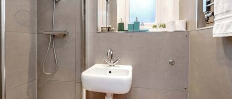A bathroom with a shower, sink, toilet, and a mirror.