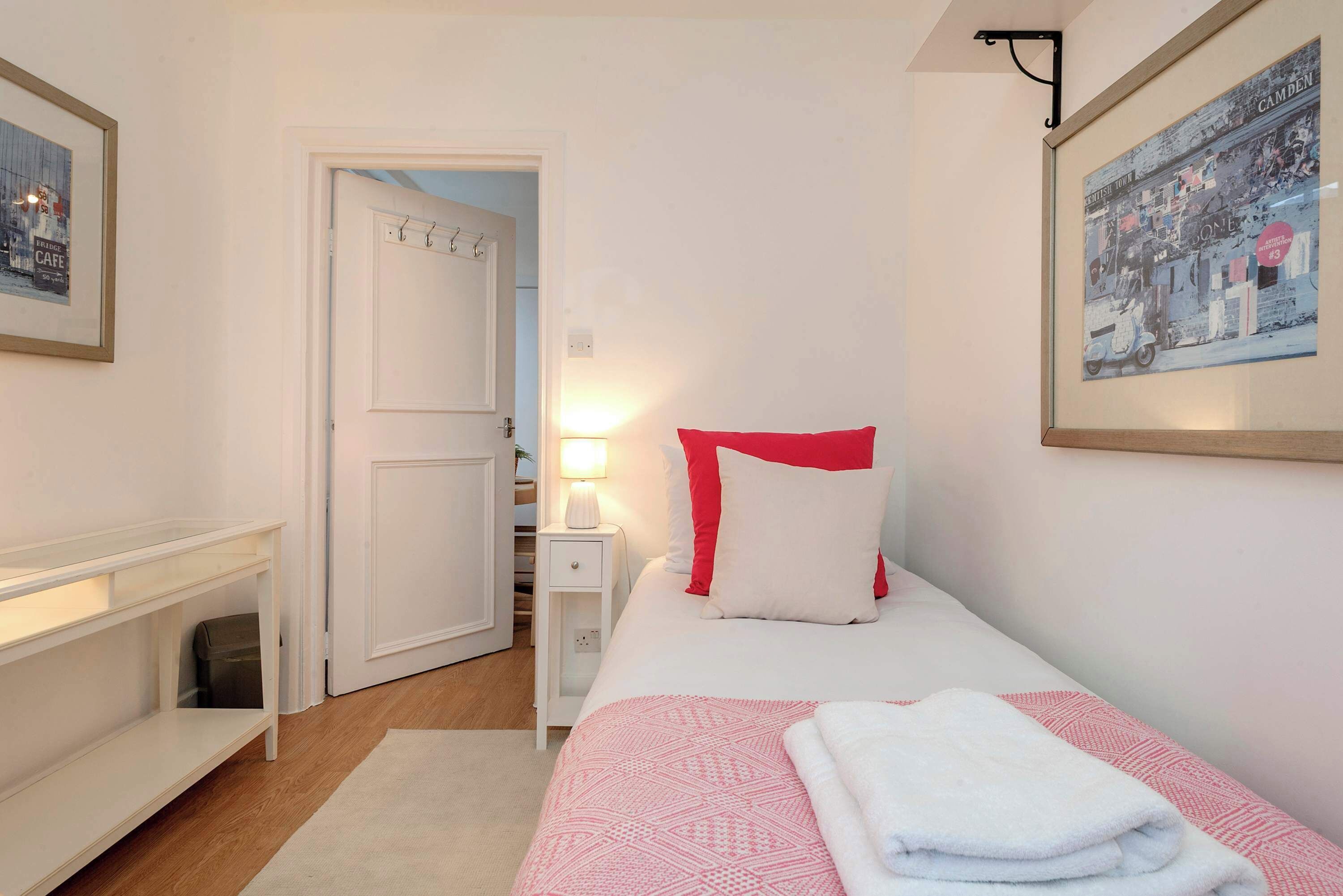 A bedroom with a bed, bedside table, nightstand, and a door leading to another room.