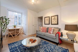 A modern living room with a grey sofa, a coffee table, a dining table with chairs, and a large window. - Stylish 2 bed - Tower Hamlets (London)