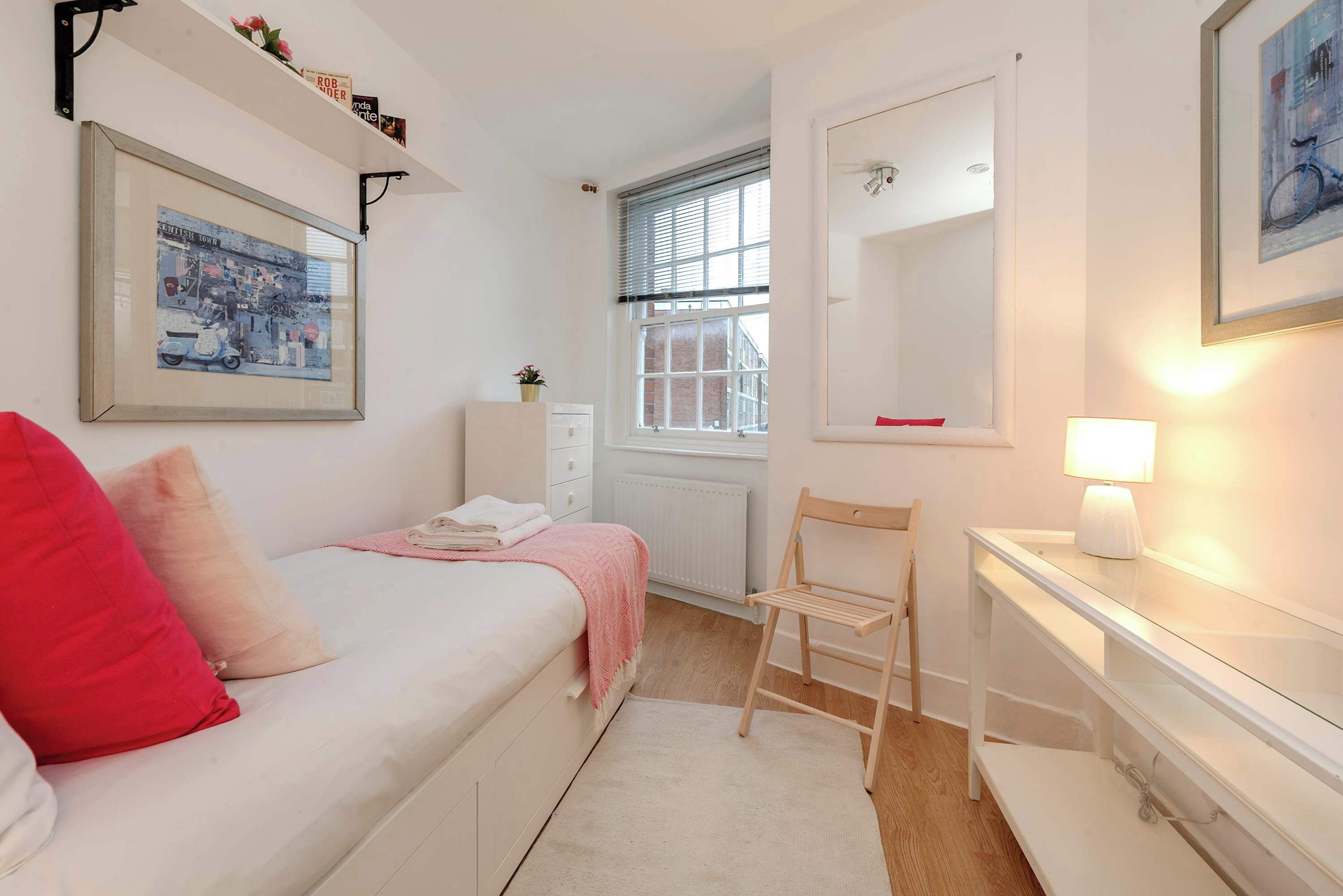 Un dormitorio con cama, una silla, una mesita de noche, una ventana y un espejo.