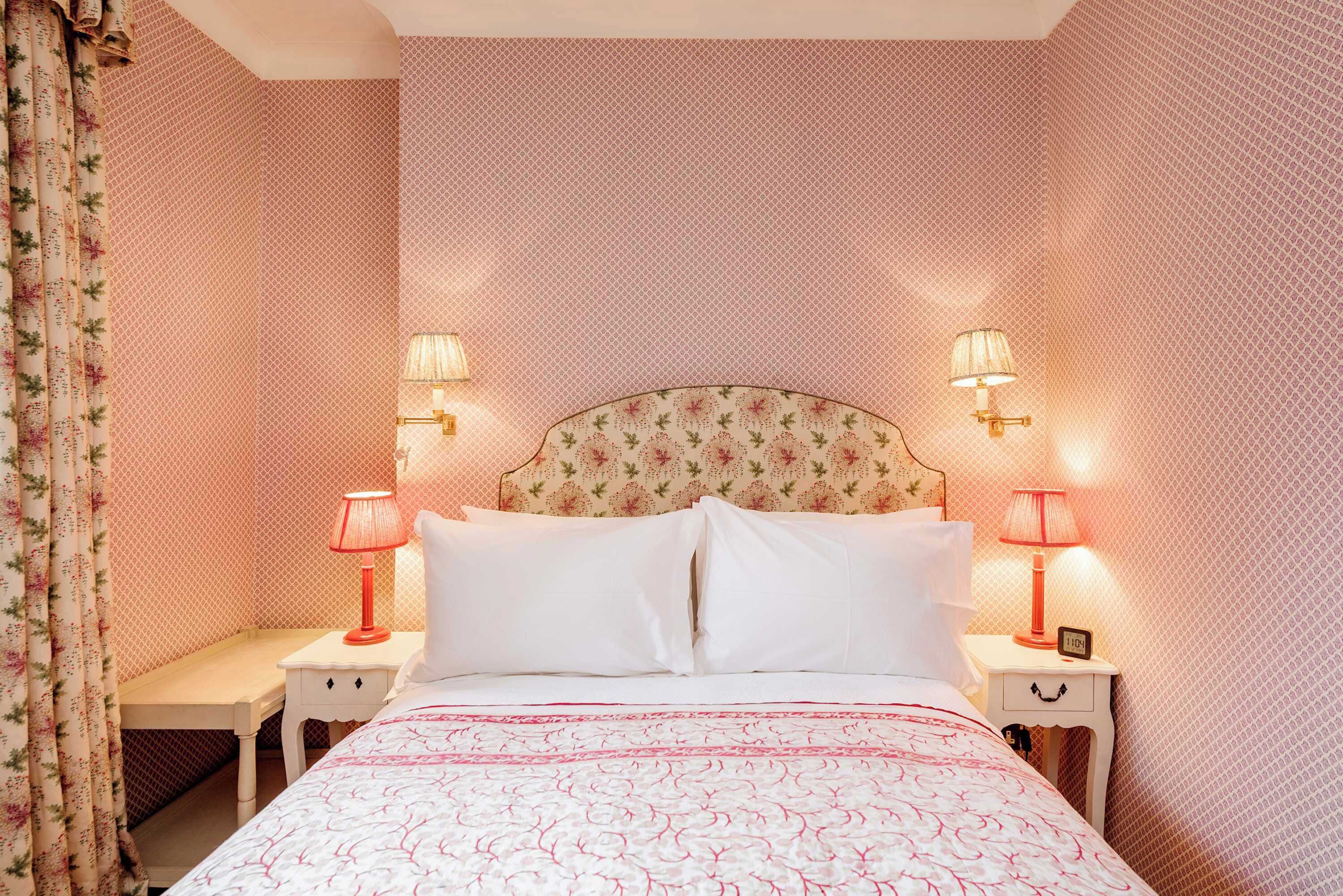 A bedroom with a floral headboard, two bedside tables with lamps, and a bed with a patterned bedspread.