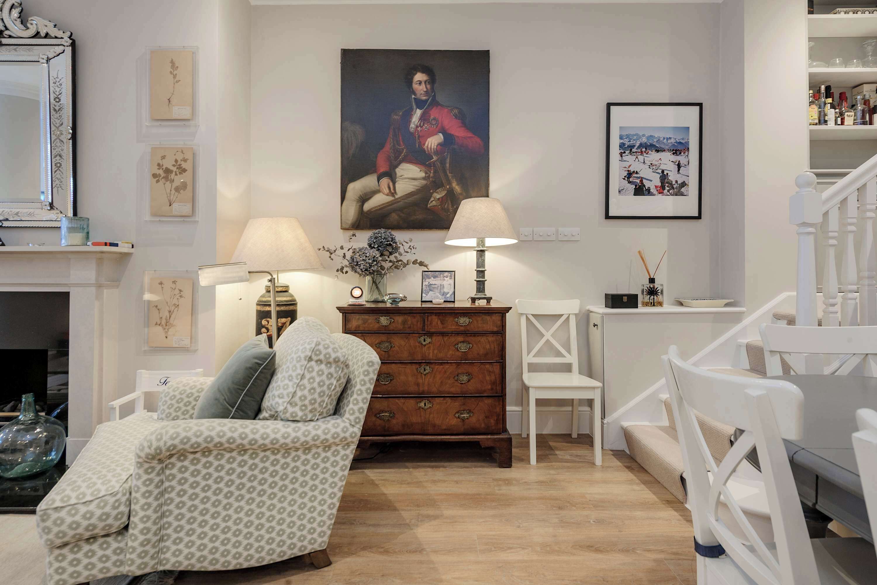 A living room with a patterned sofa, a wooden dresser, a painting of a historical figure, and a framed photograph on the wall.