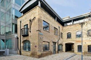 A historic building with a brick facade, large windows, and a modern glass structure adjacent to it. - Elegant 2 Bedroom Flat - King's Cross (London)