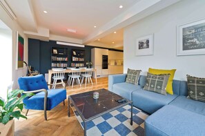 A modern living room with a blue sofa, a coffee table, and a bookshelf. - Elegant 2 Bedroom Flat - King's Cross (London)