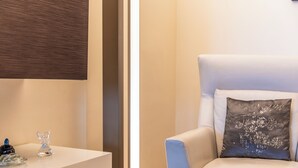 A modern room with a white armchair, a small table with decorative items, and a wall-mounted panel.