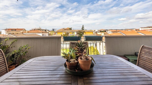 A terrace with a table, potted plants, and a view of buildings.