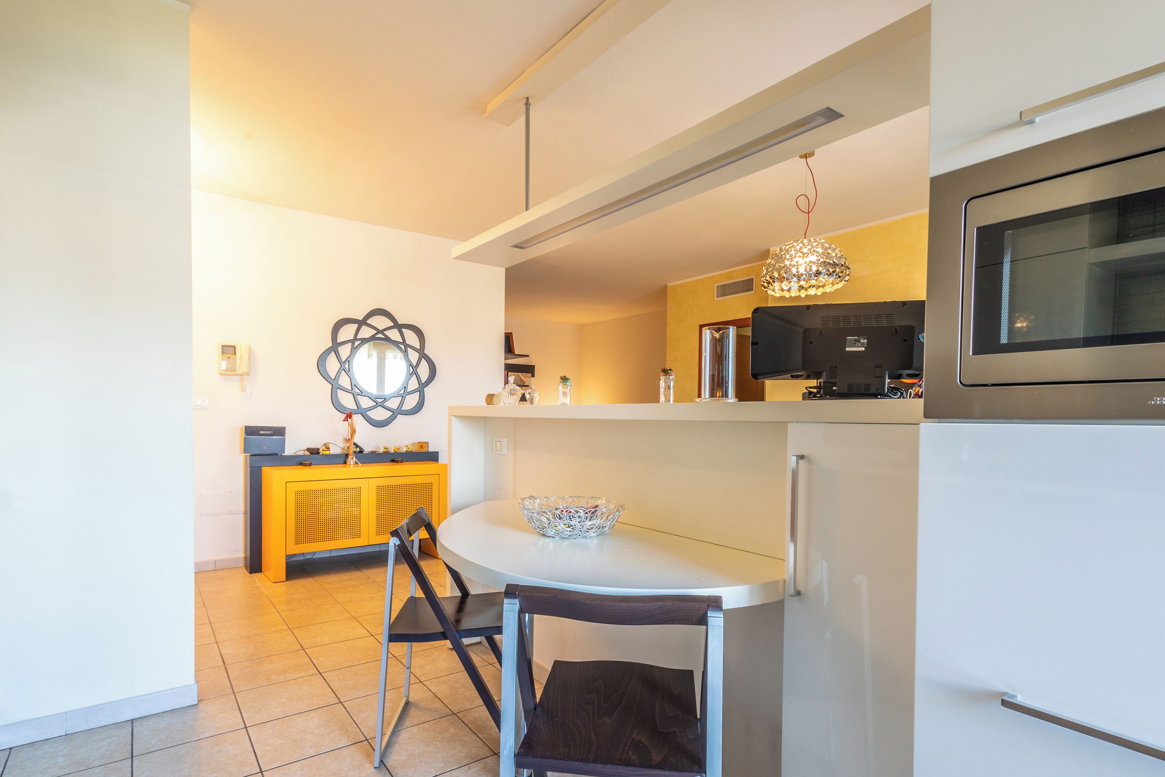 Une cuisine moderne avec un plan de travail blanc, un coin repas avec une chaise et un four encastré.