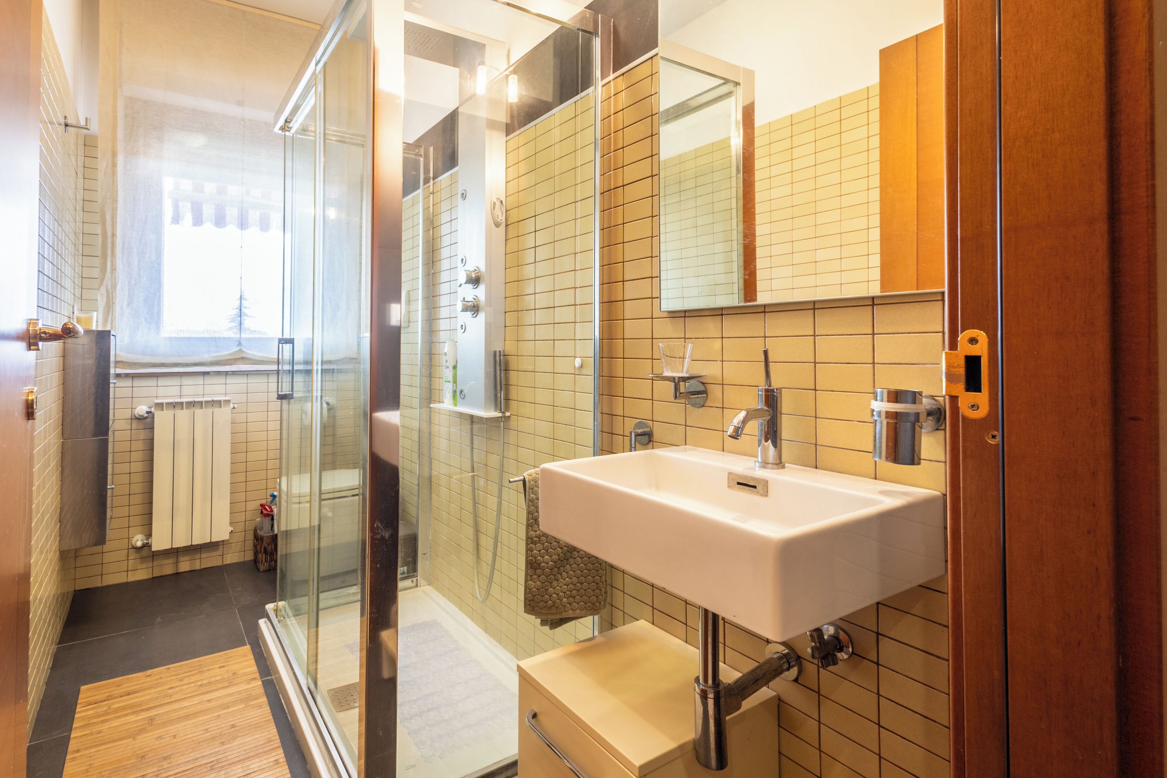 Een moderne badkamer met een douchecabine van glas, een witte wastafel en een grote spiegel.