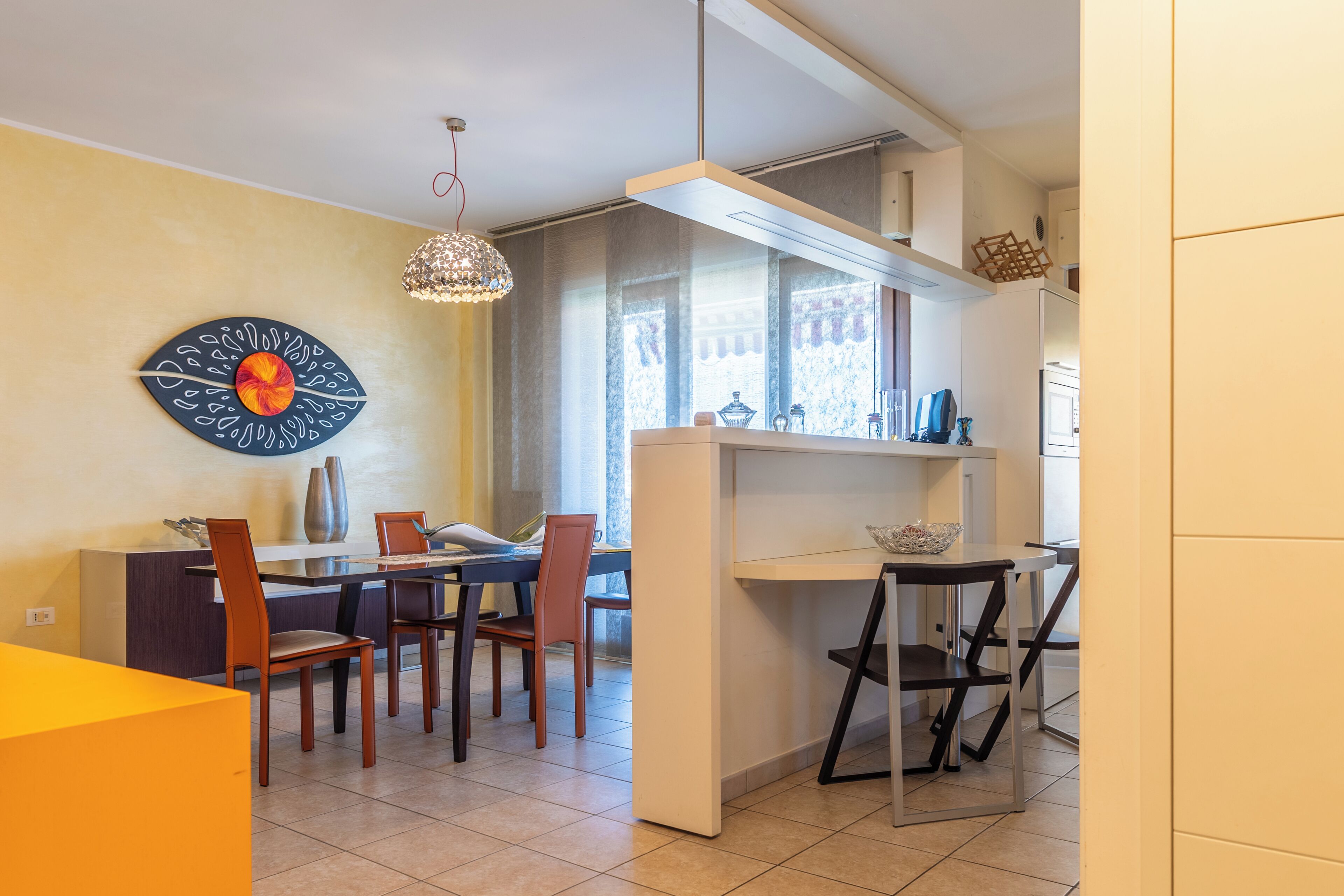 A dining area with a table, chairs, a chandelier, and a decorative wall piece.