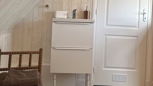 A room with a white dresser, a mirror, a door with a skateboard, and a chair with a towel.