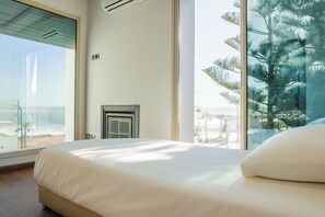 A modern hotel room with a large bed, a view of the beach, and a glass wall.
