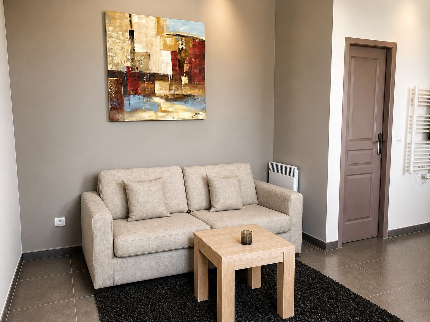 A modern living room with a beige sofa, a small wooden table, and a large abstract painting on the wall.