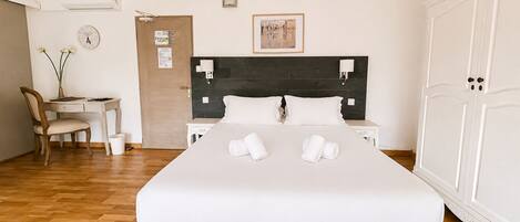 A hotel room with a bed, a desk, a chair, a wardrobe, and a wall-mounted air conditioner.