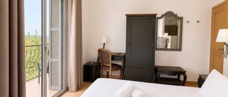 Quarto de hotel com cama, escrivaninha, guarda-roupa e varanda com cortinas.