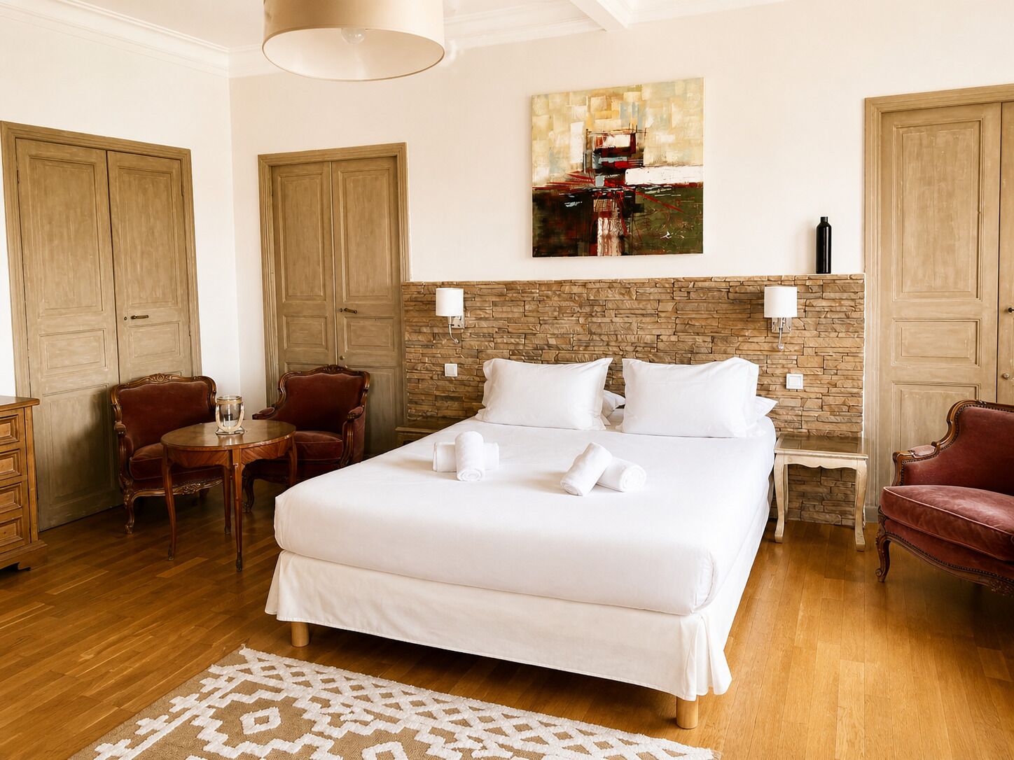 Ein Hotelzimmer mit einem großen Bett, zwei Sesseln, einem kleinen Tisch und einem Gemälde an der Wand.