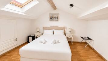 A bedroom with a large bed, two bedside tables, a nightstand, a skylight, a painting, and a folding chair.