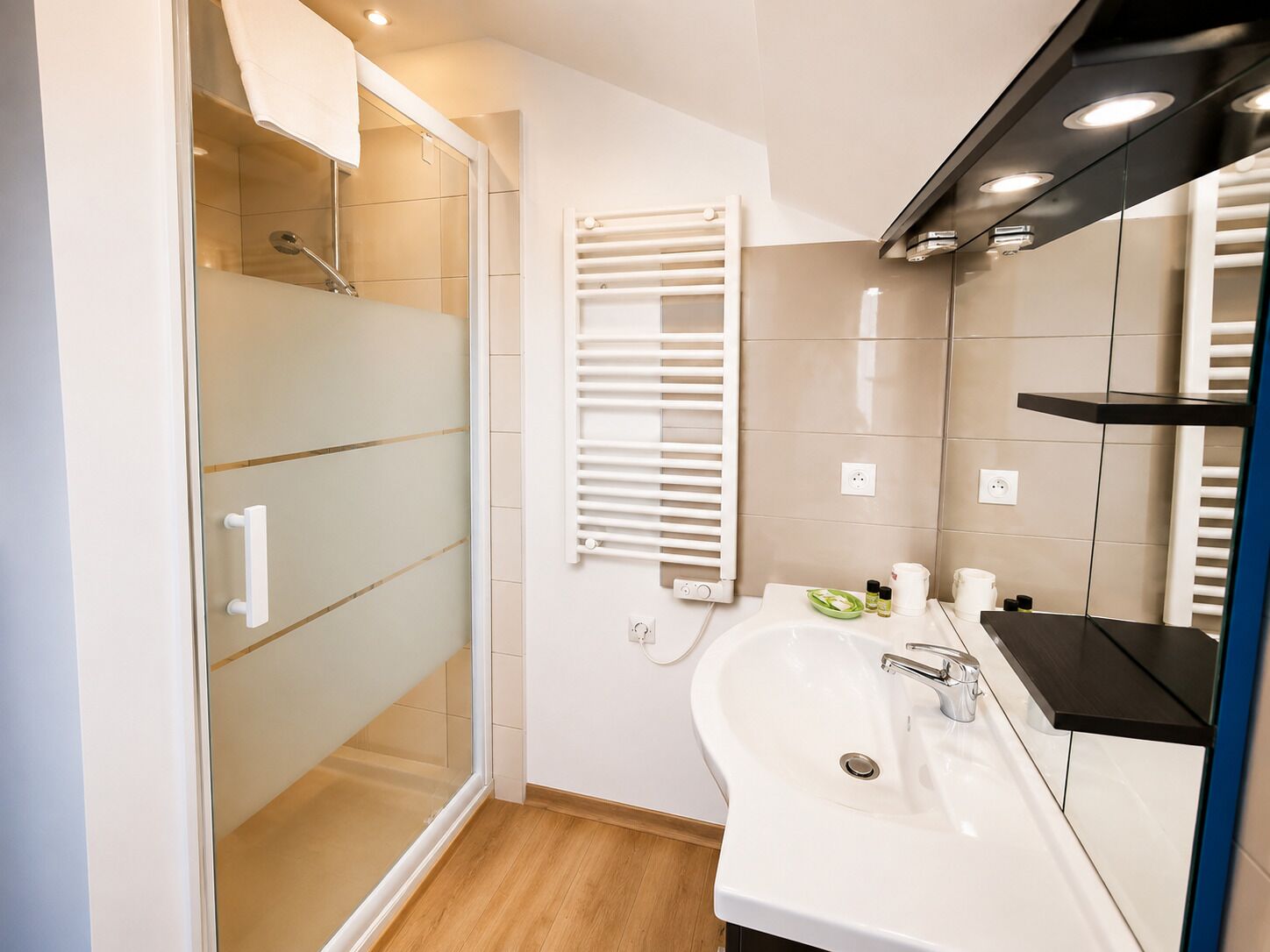 A modern bathroom with a glass shower enclosure, a white sink with a mirror, and a towel rack.