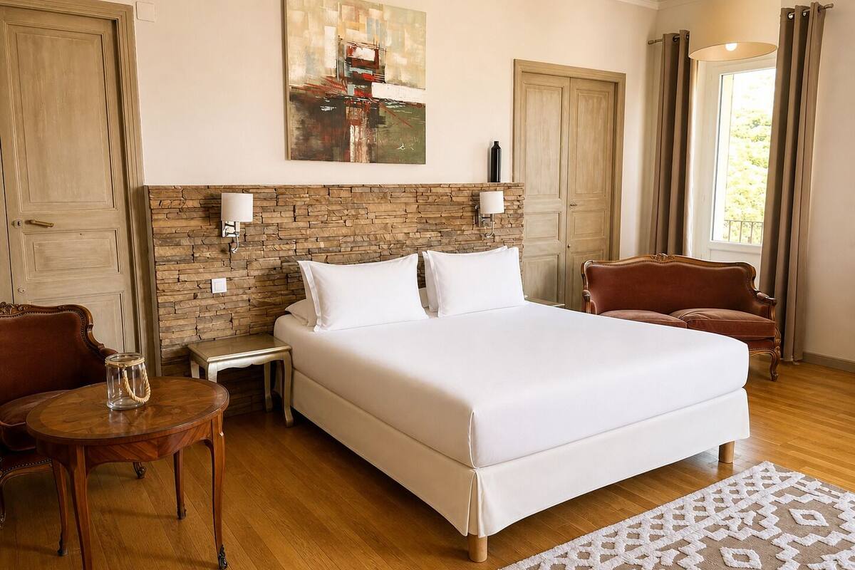 Habitación de hotel con una cama grande, un muro decorativo de piedra, un cuadro, una araña y vistas al exterior.