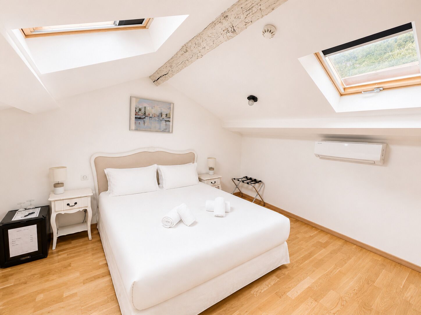 A bedroom with a bed, bedside tables, a window, an air conditioning unit, and a skylight.