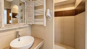 A bathroom with a white sink, a mirror with a rustic frame, a towel rack, and a shower area.