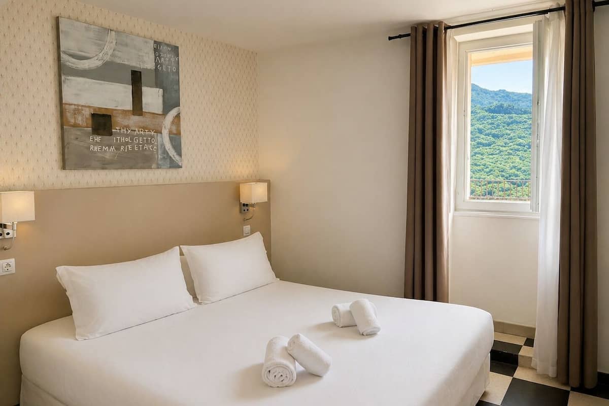 Habitación de hotel con cama, dos lámparas de noche, una ventana con cortinas y una obra de arte en la pared.