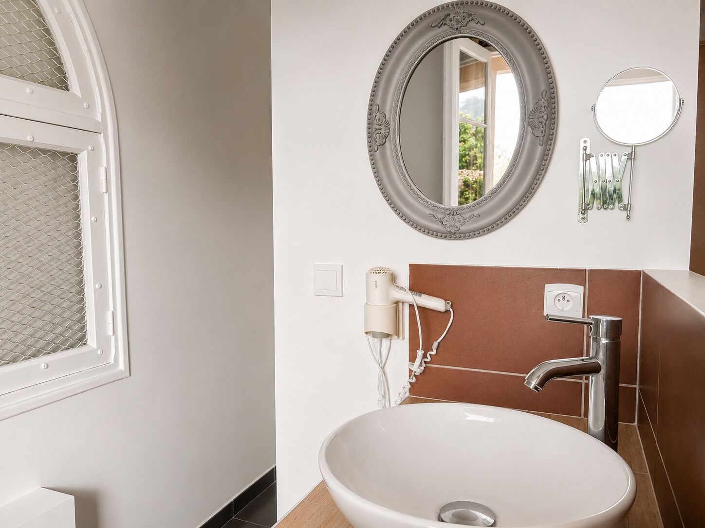 Une salle de bain avec un grand lavabo ovale, un miroir fixé au mur, un sèche-cheveux et un robinet.