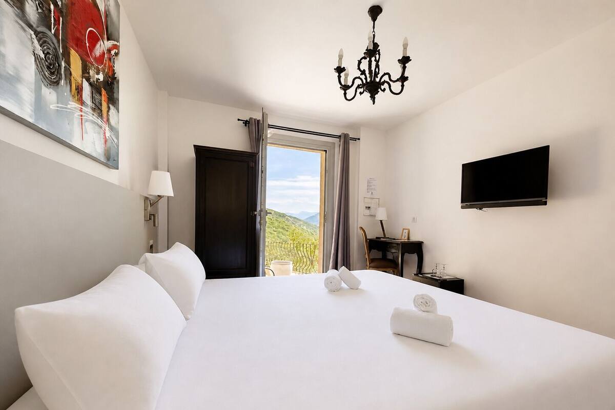 Habitación de hotel con una cama grande, un candelabro, un televisor y vistas al exterior.