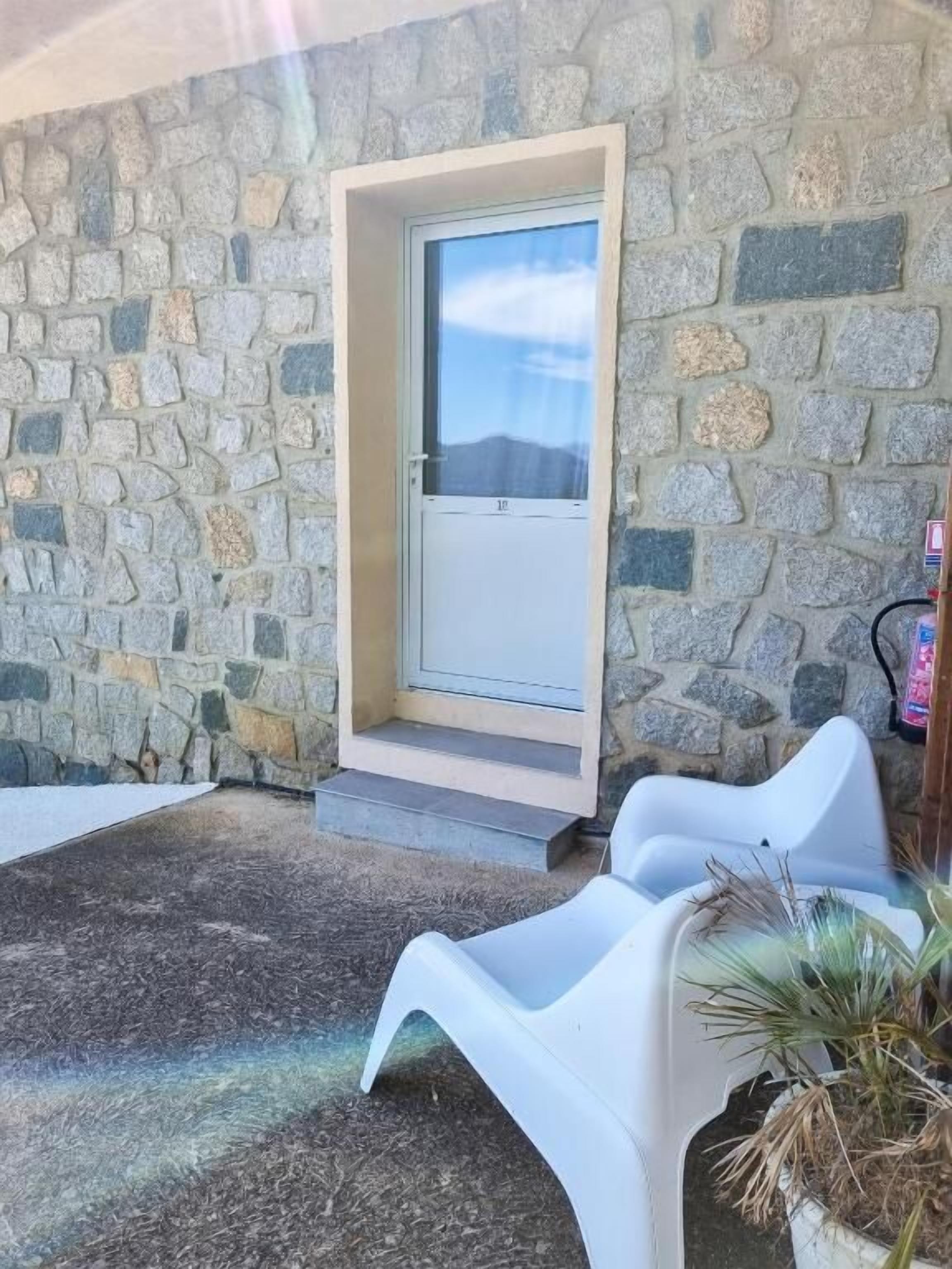 A stone building with a door, steps, and white plastic chairs.